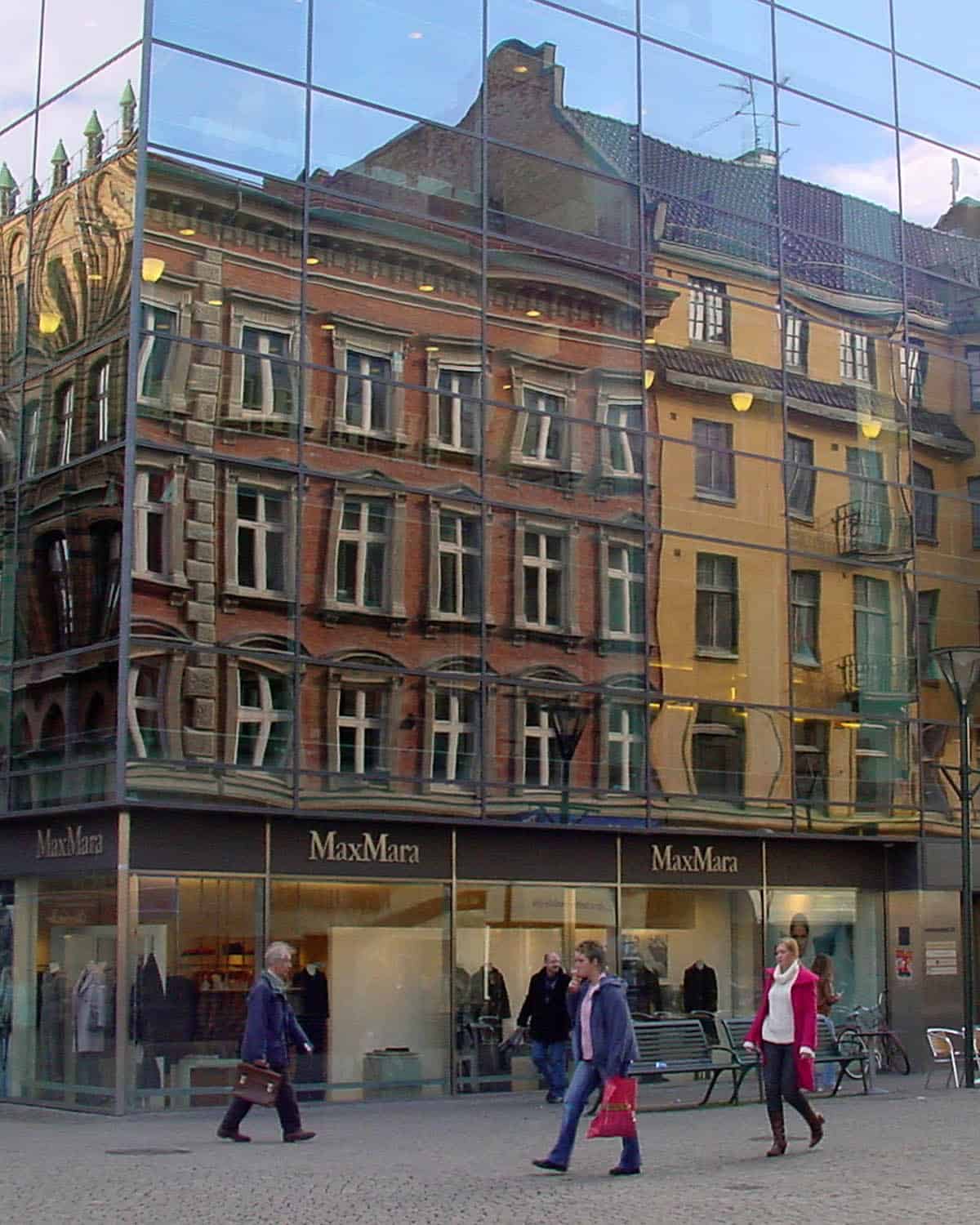 old buildings reflecting in a mirrored modern building with people walking by in Malmö, Sweden.