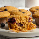 several blueberry muffins on a plate and the one in front is partially eaten.