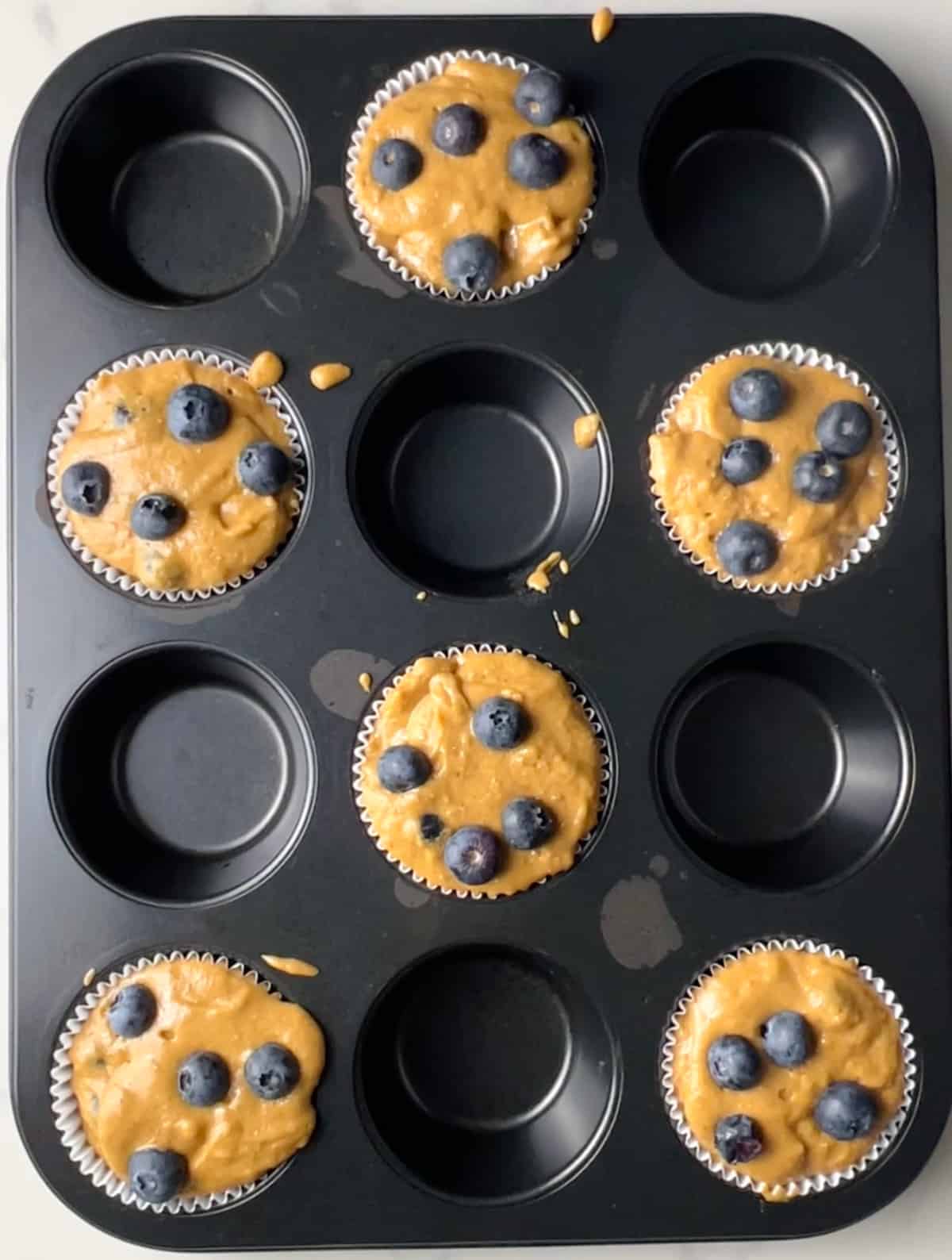 muffin pan with 6 muffins before being topped with turbinado sugar, before being baked.