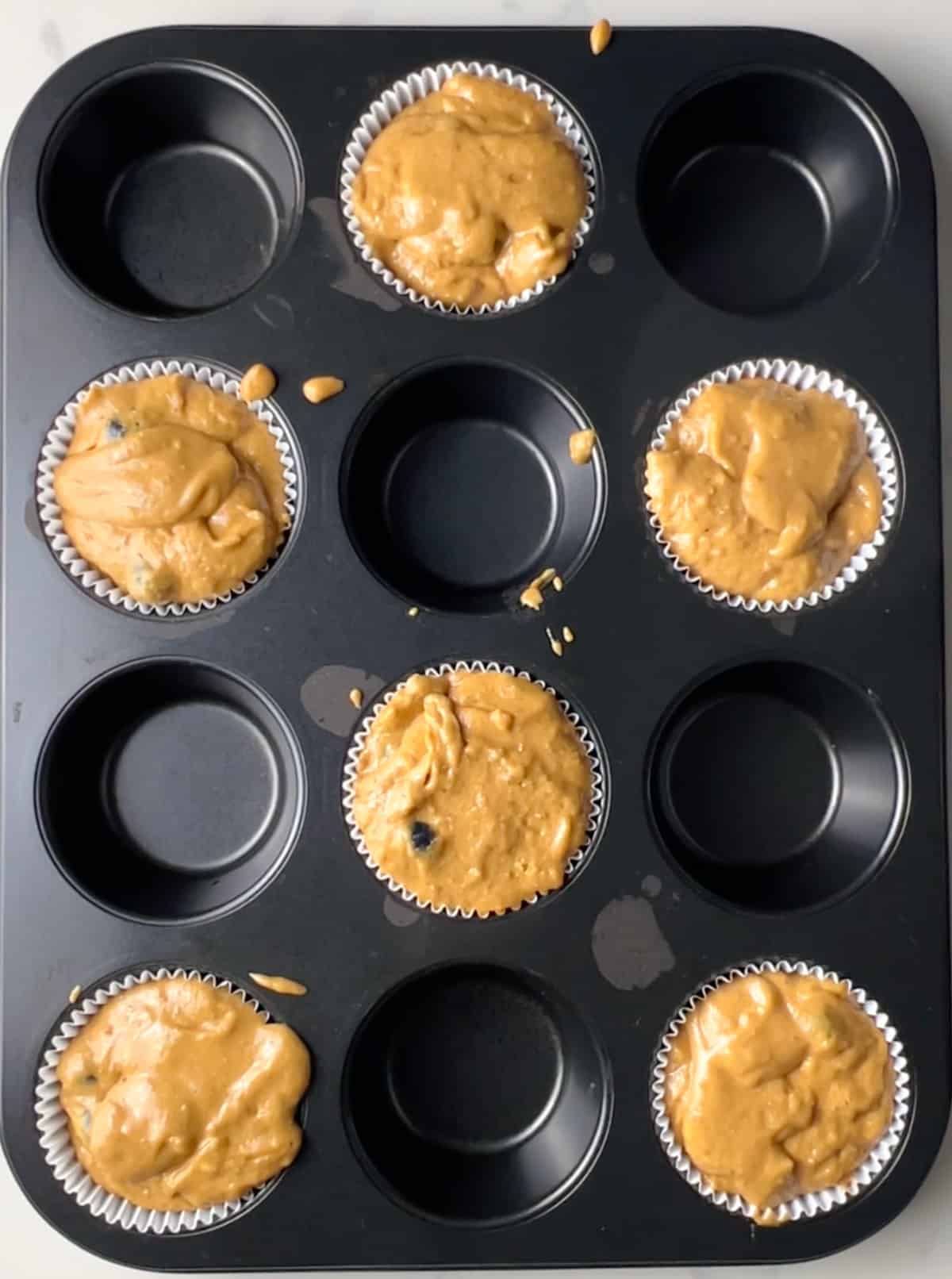 muffin pan with 6 muffins before being topped with blueberries and turbinado sugar, before being baked.